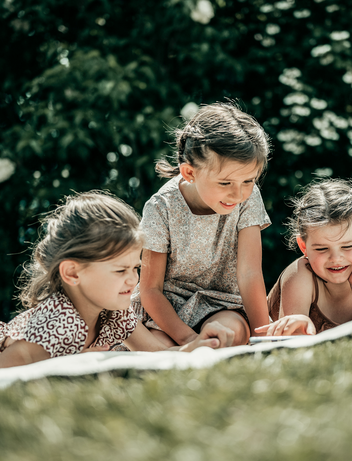 Kinder liegen auf einer Wiese und lesen ein Buch 