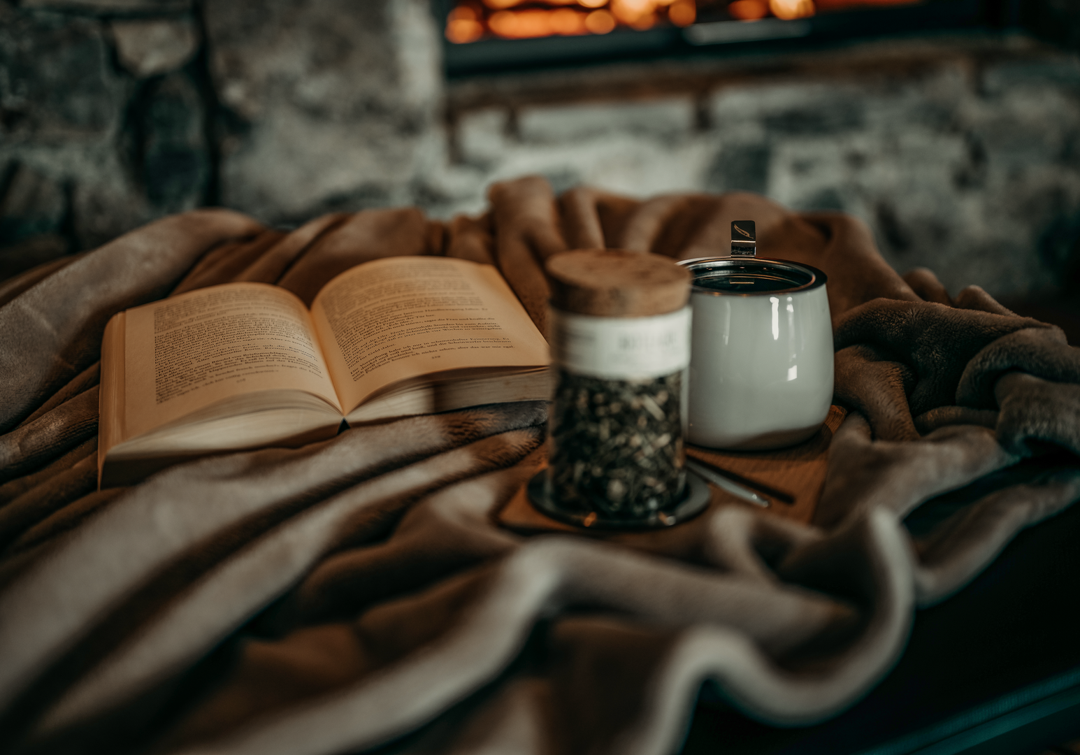 Gemütliche Winterstimmung mit offenem Buch, Kerze und warmem Getränk.