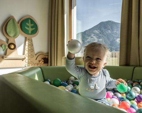 Kleinkind spielt in einem Bällebad vor einem großen Fenster mit Bergblick.