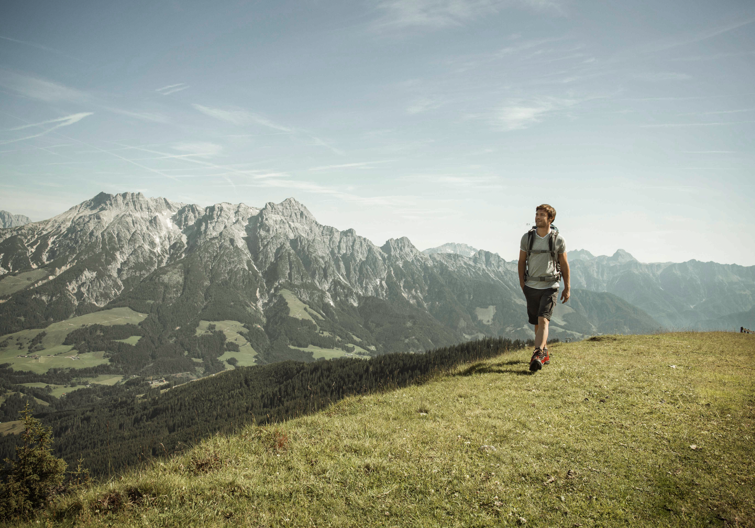 Person steht auf einem Bergplateau und blickt auf die umliegende Berglandschaft.
