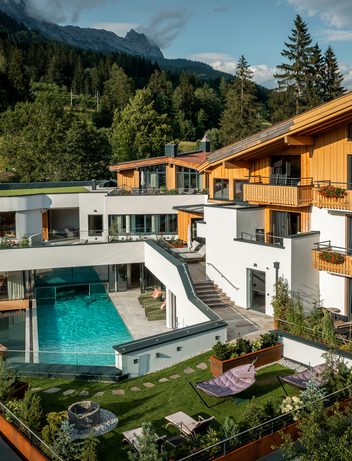 Hotelanlage mit Poolbereich, Garten und alpiner Kulisse.