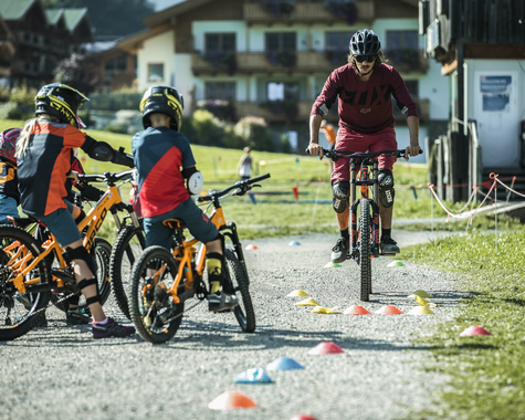 Jugendliche und Kinder fahren mit Fahrrädern auf einem Übungsparcours im Außenbereich einer Ferienanlage.