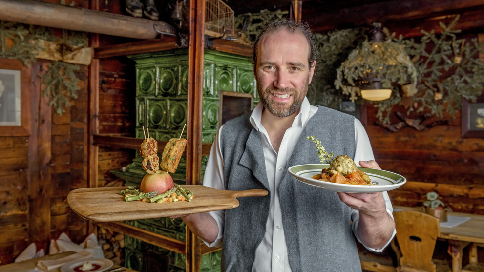 Person präsentiert regionale Speisen in einem rustikal eingerichteten Restaurant.