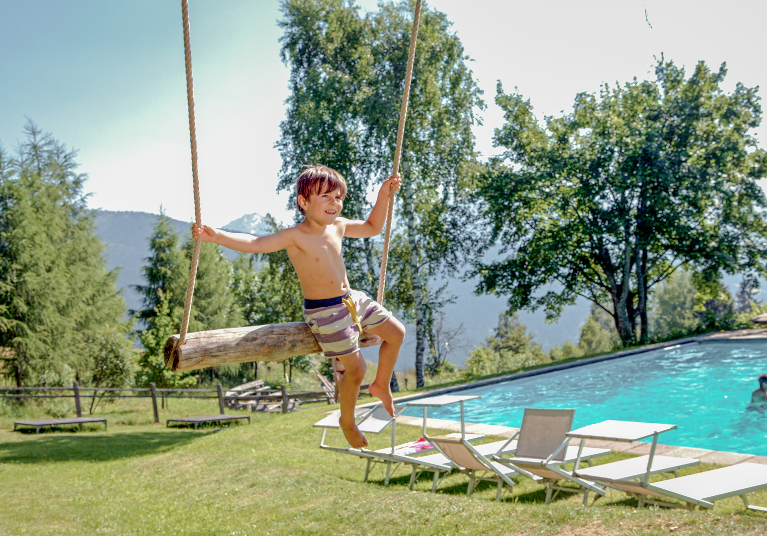 Kind schwingt auf einer Schaukel vor einem Pool 