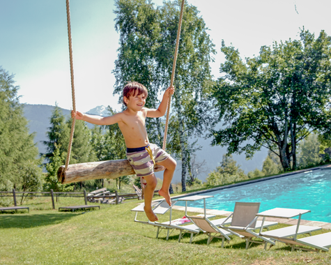 Kind schwingt auf einer Schaukel vor einem Pool 