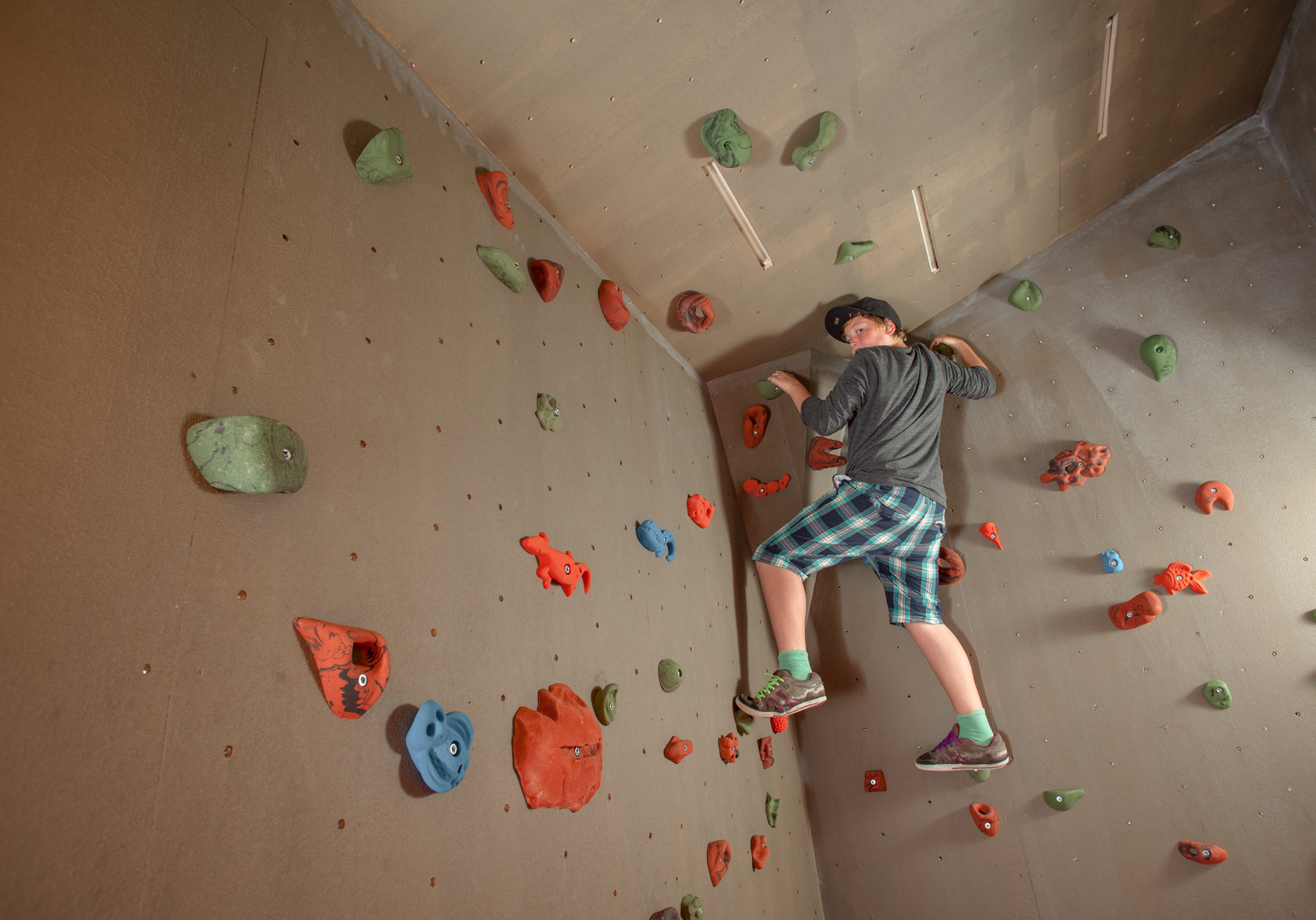 Kind klettert an einer Indoor-Kletterwand mit bunten Griffen.