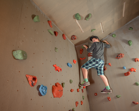 Kind klettert an einer Indoor-Kletterwand mit bunten Griffen.