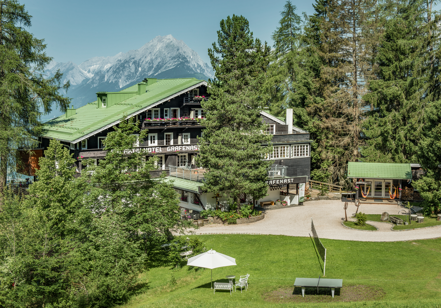 Ferienhaus mit Garten und Spielbereich vor einer alpinen Bergkulisse.
