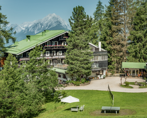 Ferienhaus mit Garten und Spielbereich vor einer alpinen Bergkulisse.