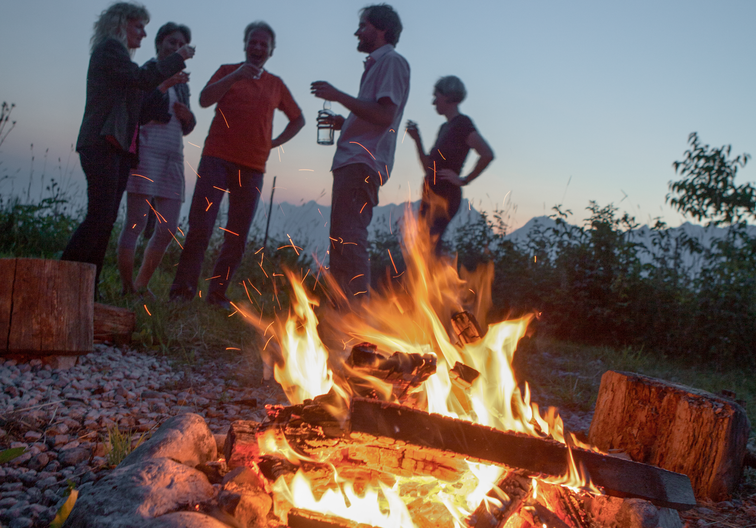 Kinder und Erwachsene sitzen gemeinsam an einer Feuerstelle im Freien.