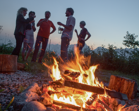 Kinder und Erwachsene sitzen gemeinsam an einer Feuerstelle im Freien.