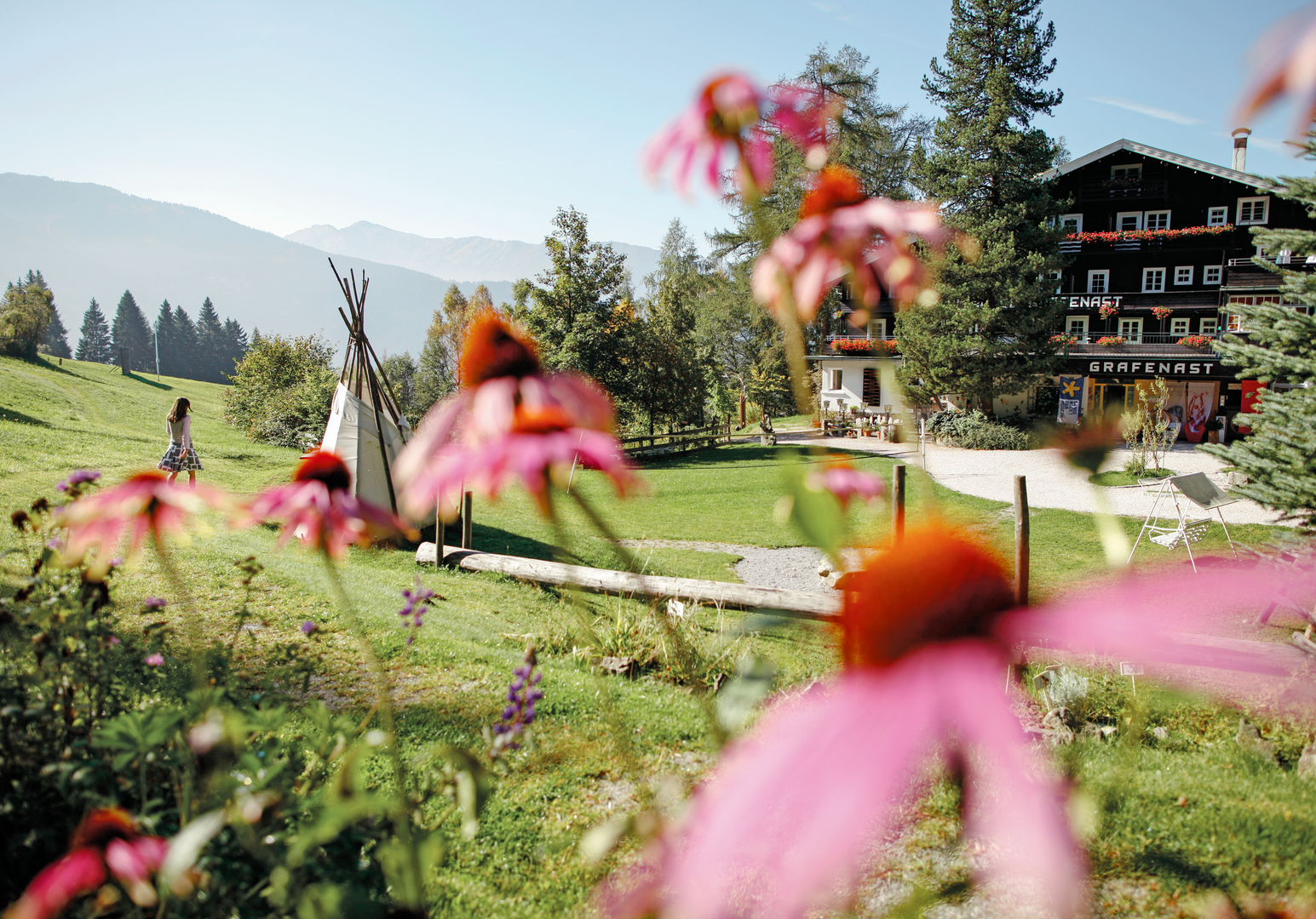 Blühender Garten mit Blick auf eine Berglandschaft und ein Hotelgebäude.