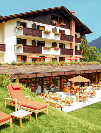 Hotel mit Gartenbereich und Liegewiese vor einer Berglandschaft.