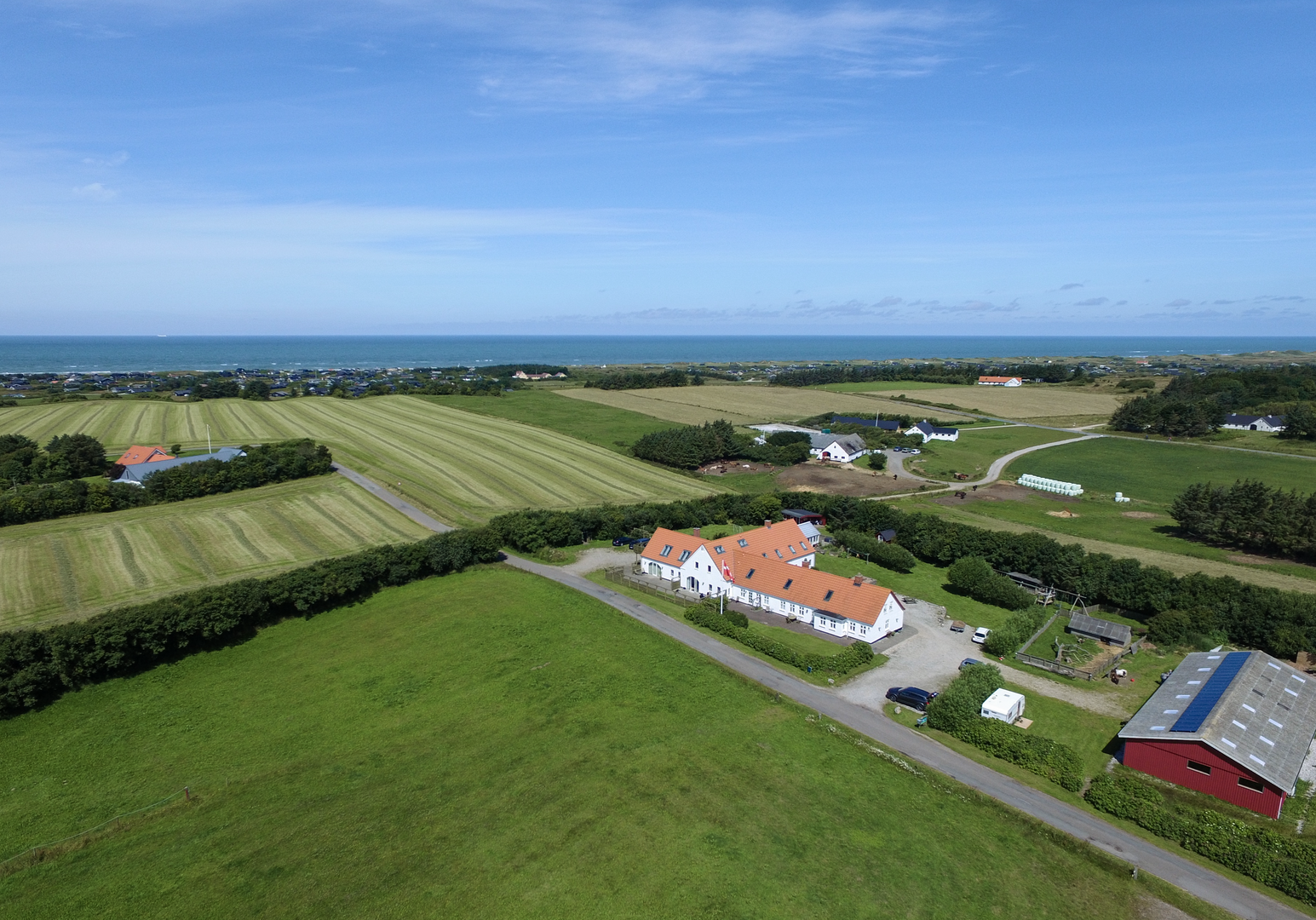 Luftaufnahme eines Bauernhofs mit roten Dächern, umgeben von grünen Feldern und ländlicher Landschaft
