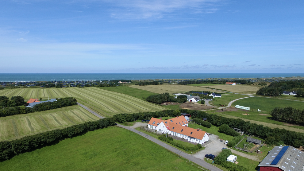 Luftaufnahme eines Bauernhofs mit roten Dächern, umgeben von grünen Feldern und ländlicher Landschaft
