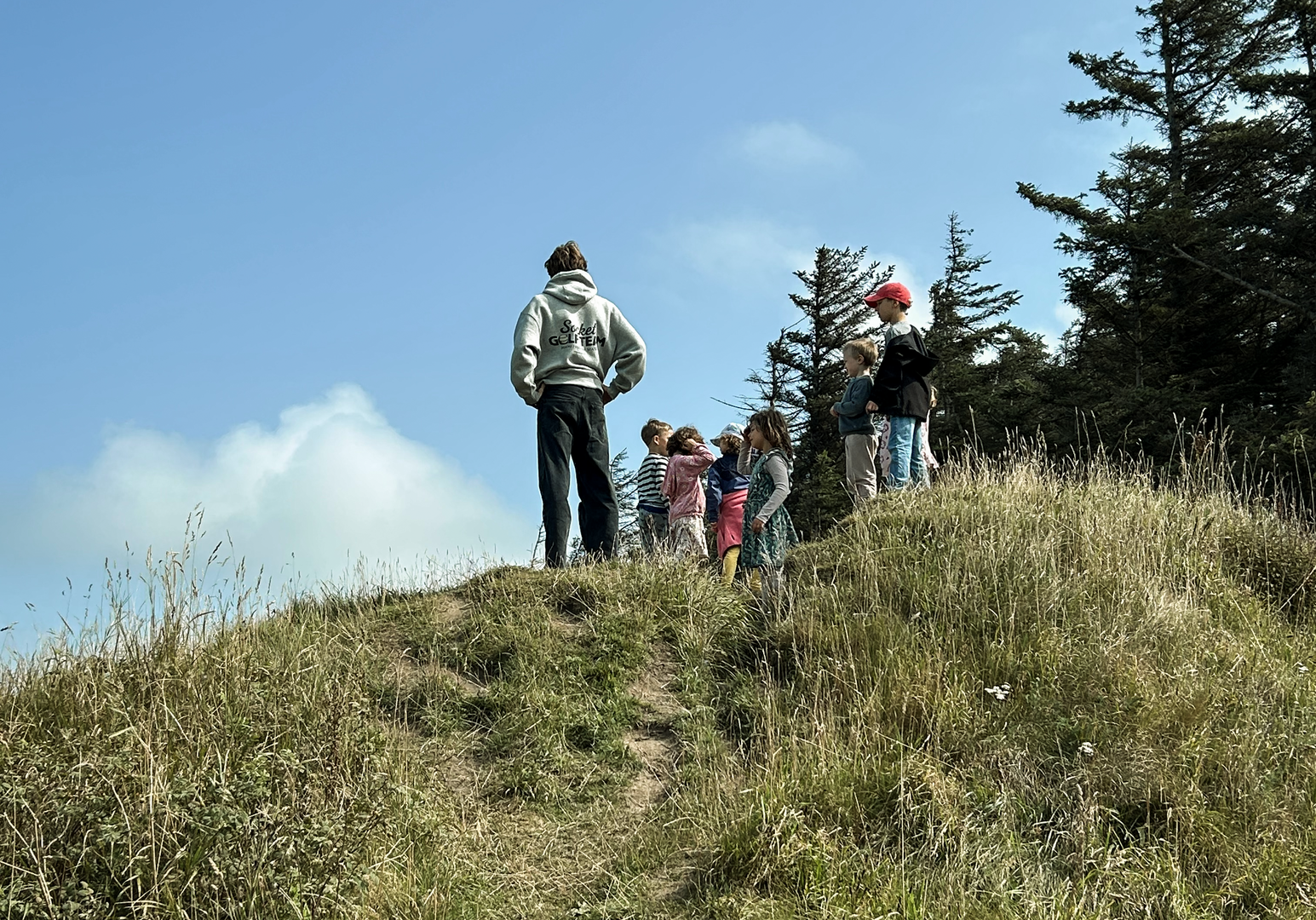 Zwei Personen stehen auf einer Anhöhe und blicken in die Ferne unter blauem Himmel