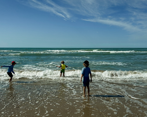 Drei Kinder spielen im flachen Wasser am Strand bei sonnigem Wetter und Wellen