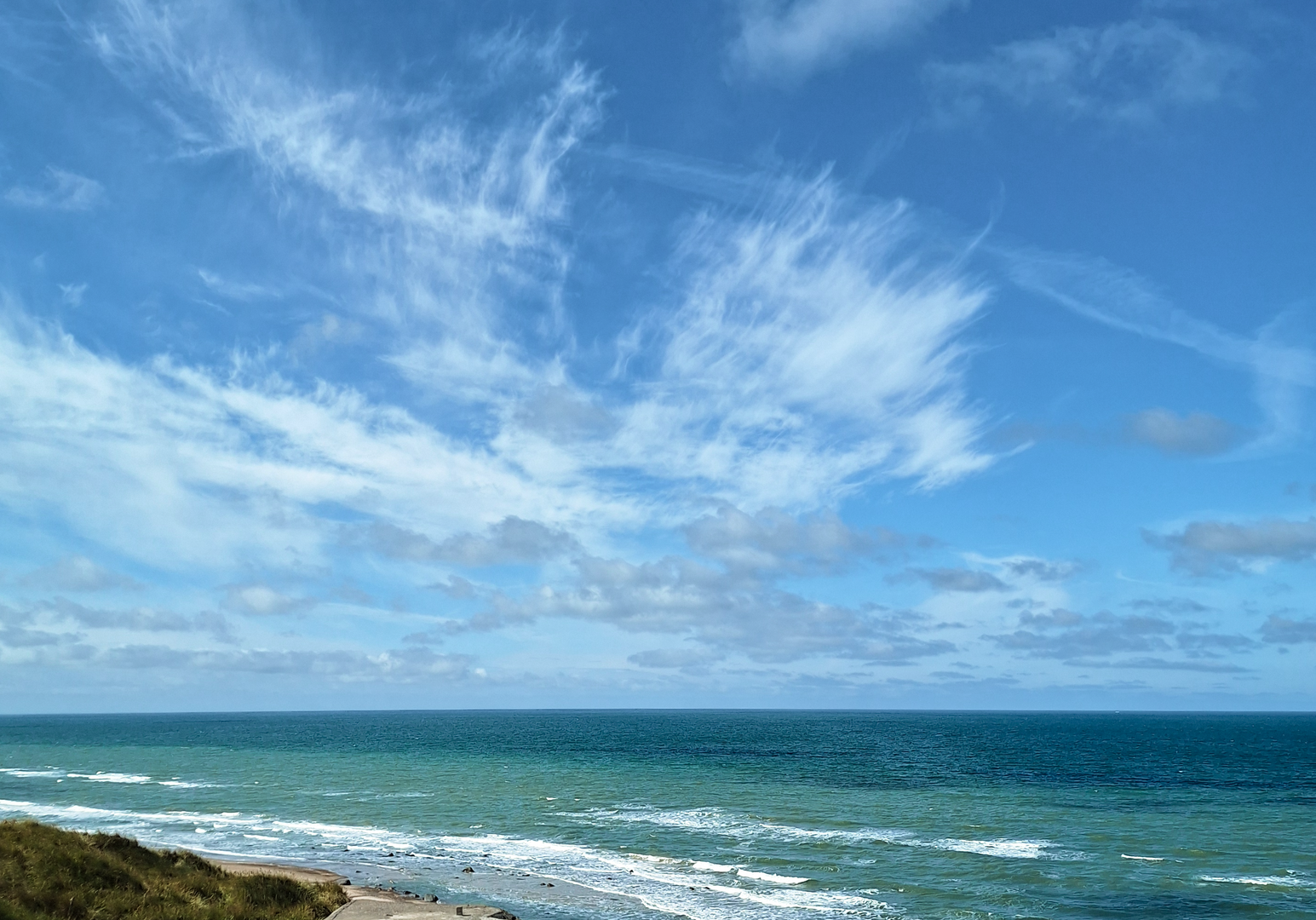Eine Küste mit Sandstrand, Meer und blauem Himmel mit leichten Wolken