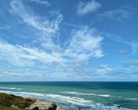 Eine Küste mit Sandstrand, Meer und blauem Himmel mit leichten Wolken