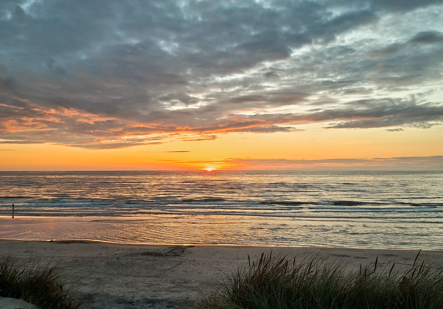 Sonnenuntergang über dem Meer mit orangefarbenem Himmel und Dünen im Vordergrund