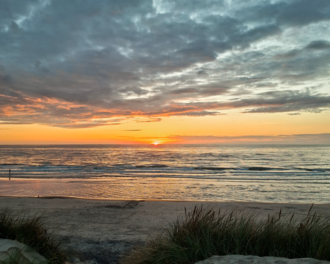 Sonnenuntergang über dem Meer mit orangefarbenem Himmel und Dünen im Vordergrund