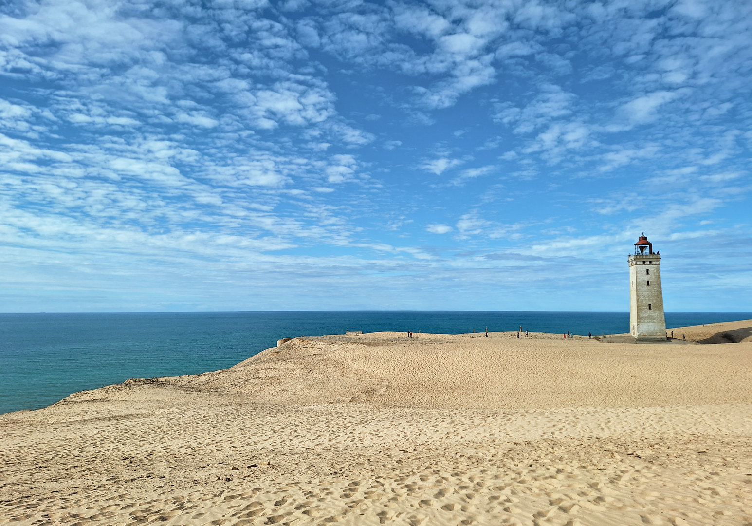 Leuchtturm auf einer sandigen Düne mit Blick auf das Meer unter blauem Himmel