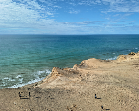 Küste mit sandigen Klippen und Blick auf das ruhige Meer unter blauem Himmel