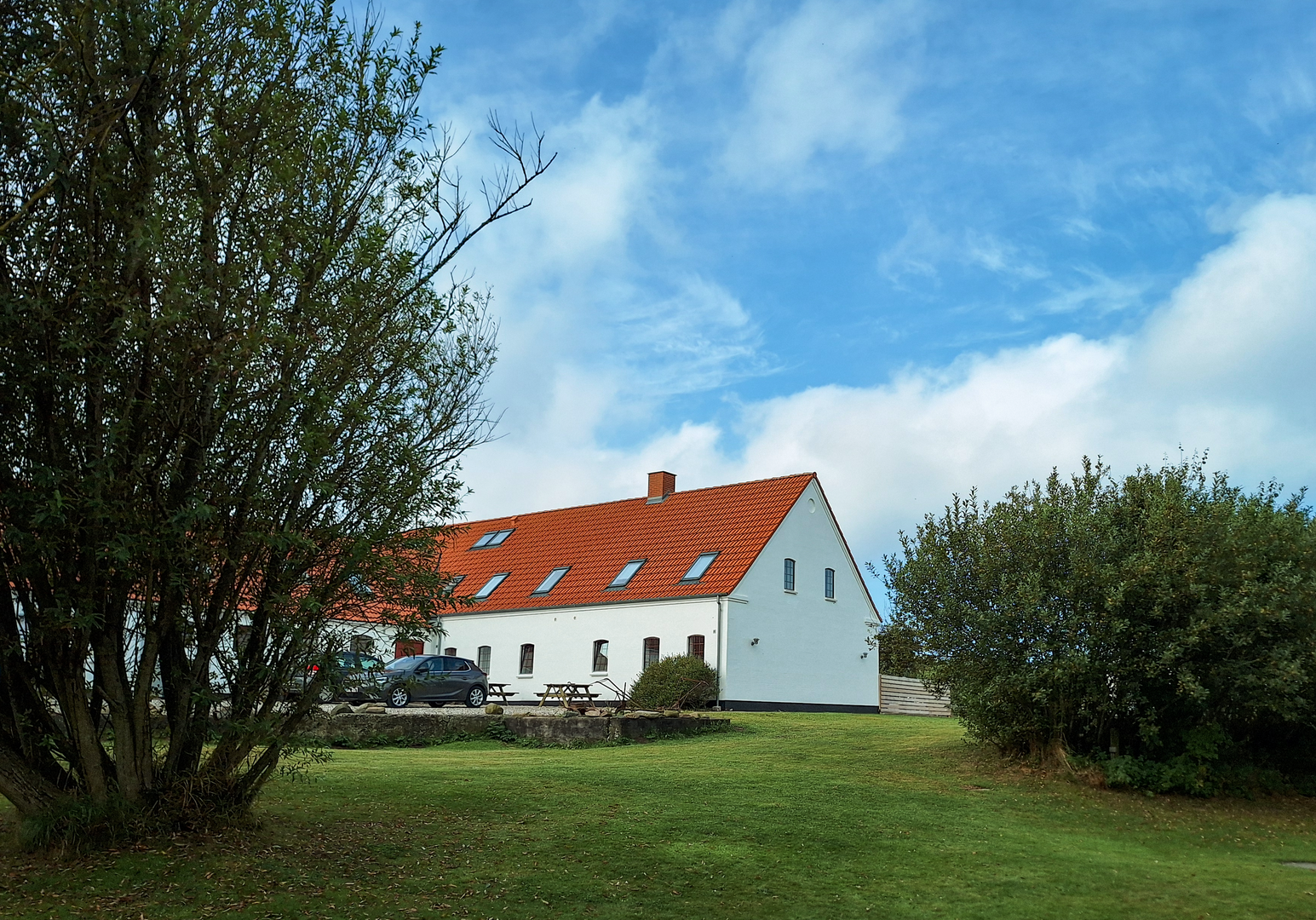 Bauernhof mit weißen Gebäuden und rotem Dach, umgeben von Bäumen und grüner Wiese