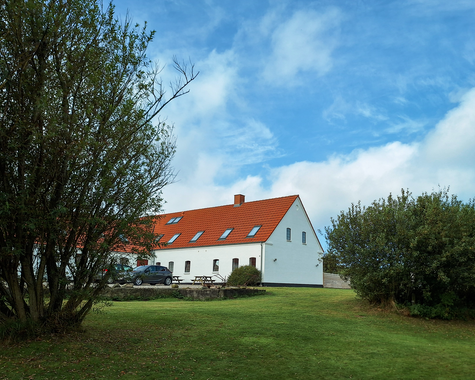 Bauernhof mit weißen Gebäuden und rotem Dach, umgeben von Bäumen und grüner Wiese