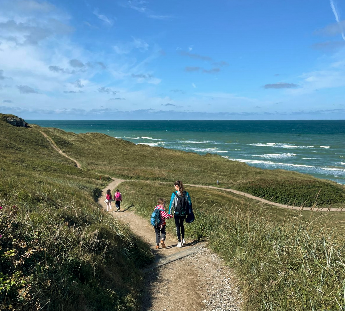 Menschen wandern auf einem schmalen Pfad durch Dünenlandschaft entlang der Küste