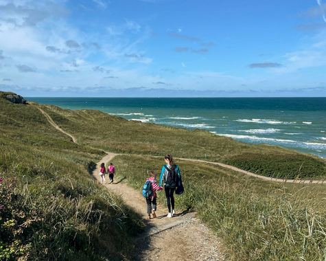 Menschen wandern auf einem schmalen Pfad durch Dünenlandschaft entlang der Küste