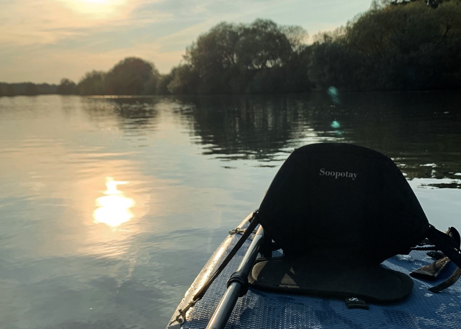 Sonnenuntergang über einem ruhigen Fluss, aufgenommen vom Boot mit Spiegelung im Wasser 