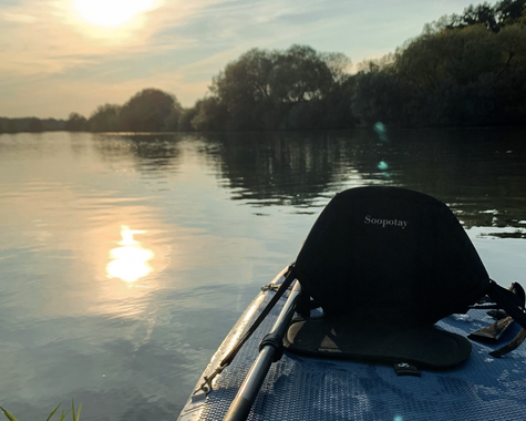 Sonnenuntergang über einem ruhigen Fluss, aufgenommen vom Boot mit Spiegelung im Wasser 