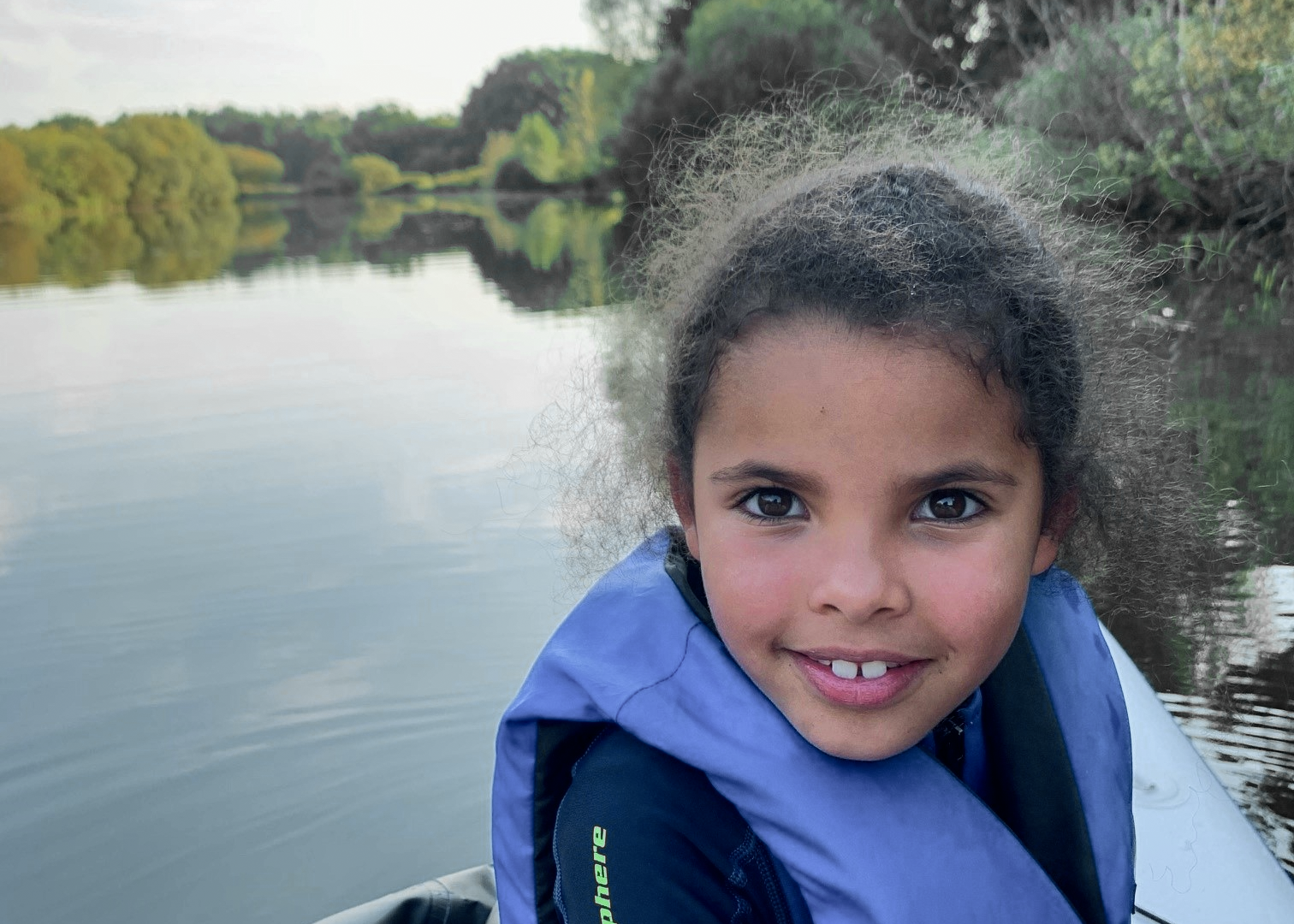 Kind mit Schwimmweste sitzt in einem Boot auf dem Fluss und schaut in die Kamera