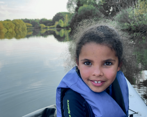 Kind mit Schwimmweste sitzt in einem Boot auf dem Fluss und schaut in die Kamera