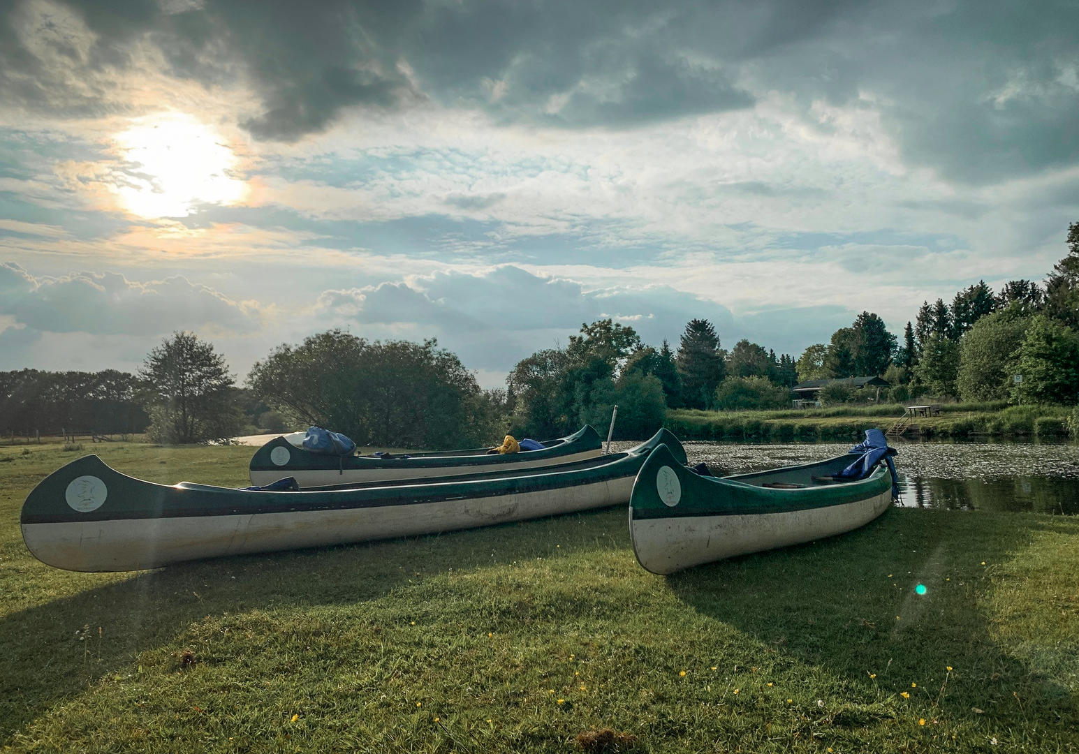 Mehrere Kanus liegen am grasbewachsenen Ufer eines Flusses im warmen Abendlicht 