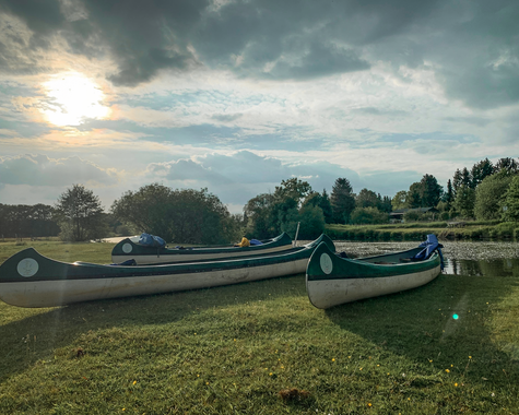 Mehrere Kanus liegen am grasbewachsenen Ufer eines Flusses im warmen Abendlicht 