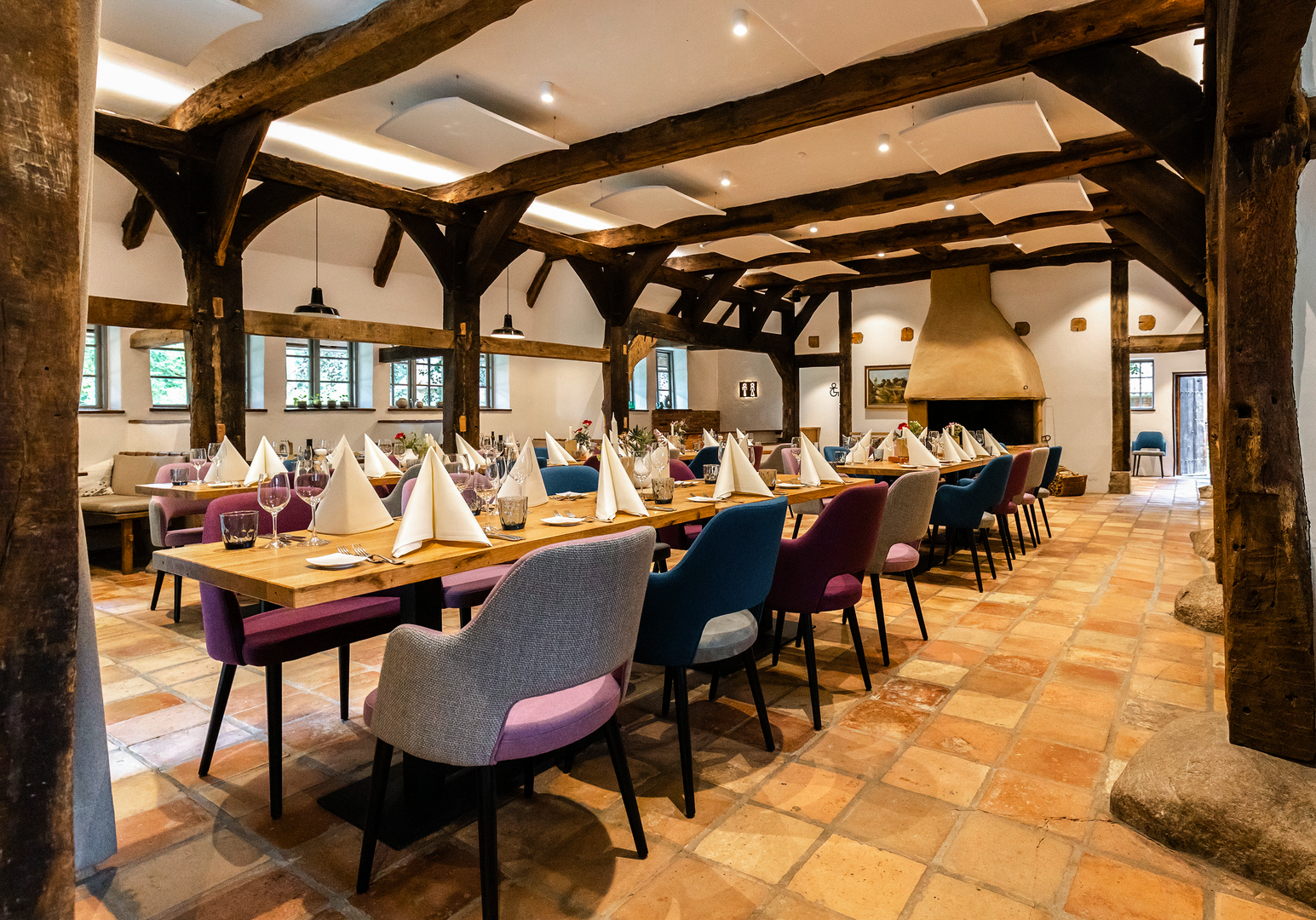 Rustikaler, gemütlicher Speiseraum mit langen Tischen, bunten Stühlen und Holzbalkendecke