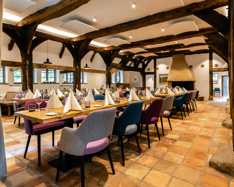 Rustikaler, gemütlicher Speiseraum mit langen Tischen, bunten Stühlen und Holzbalkendecke