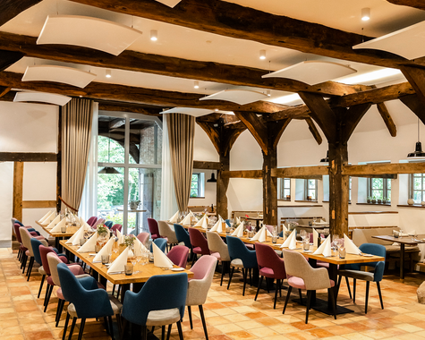 Heller Gastraum mit zentralem Tisch, großen Fenstern und sichtbaren Holzbalken