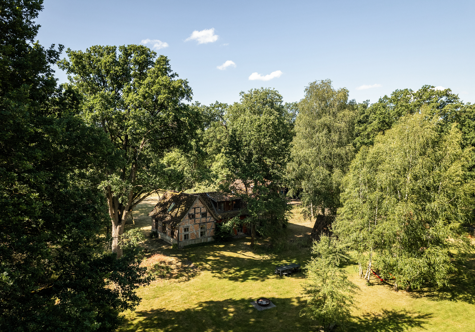 Weitläufige grüne Landschaft mit Bäumen und einem Haus im Hintergrund