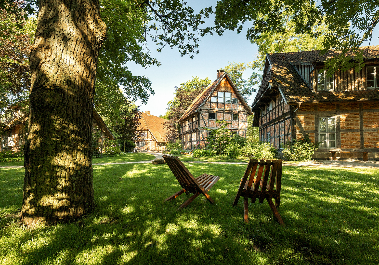 Garten mit Liegestühlen unter Bäumen vor Fachwerkgebäuden