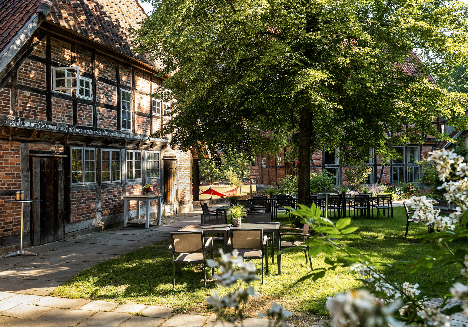 Garten mit Picknicktischen vor einem Fachwerkhaus im Schatten großer Bäume