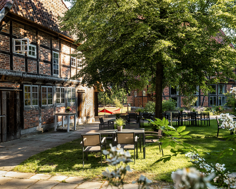 Garten mit Picknicktischen vor einem Fachwerkhaus im Schatten großer Bäume