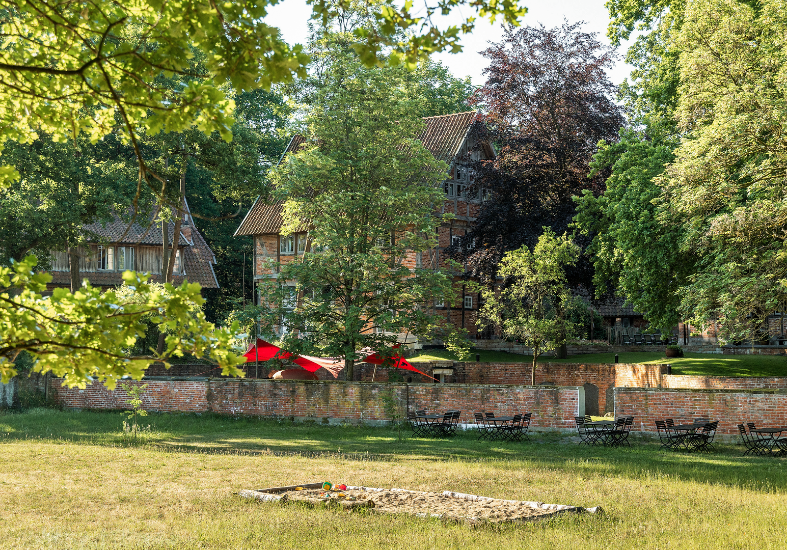 Garten mir Bänken und einer Sandkiste und einer Mauer mit Haus im Hintergrund