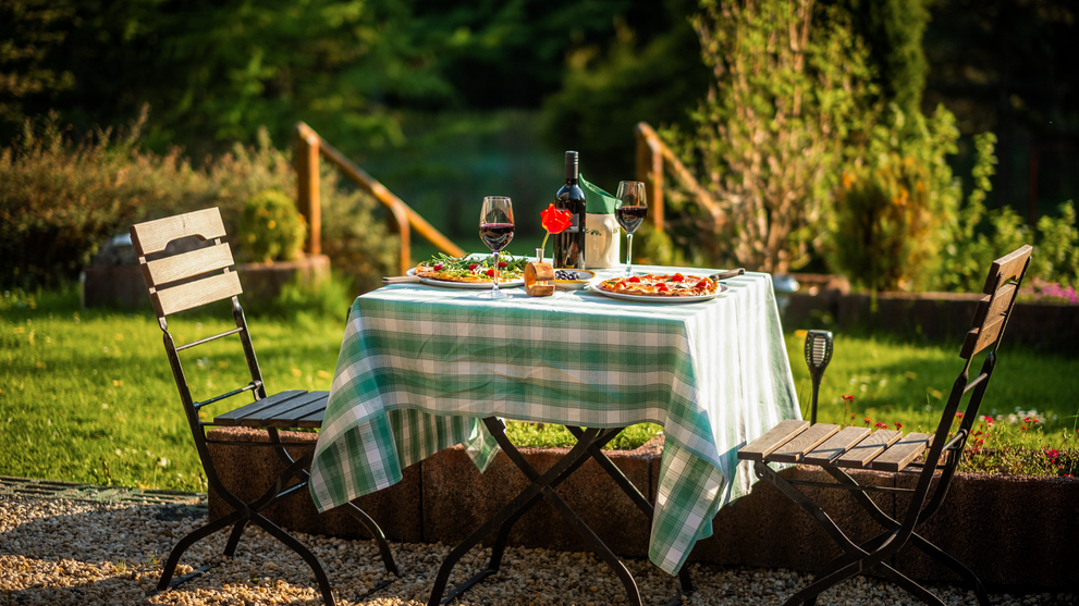 Gartentisch mit kariertem Tischtuch und Stühlen im Abendlicht