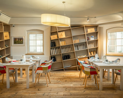 Heller Frühstücksraum mit Tischen, Stühlen und Bücherregalen