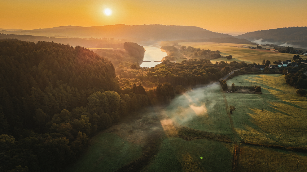 Sonnenaufgang über einer Flusslandschaft mit Hügeln und Feldern
