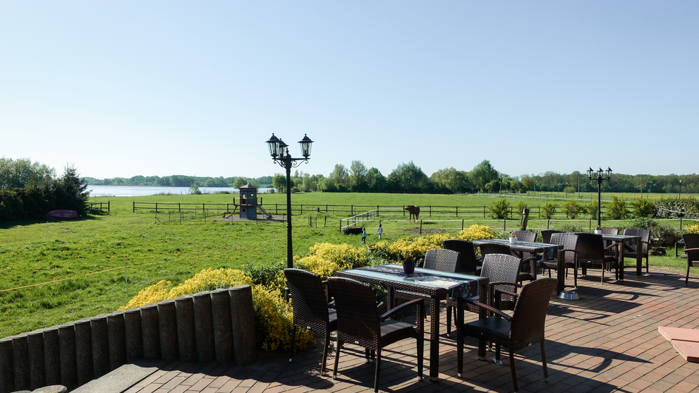 Terrasse mit Tischen und Stühlen mit Blick über weite Felder