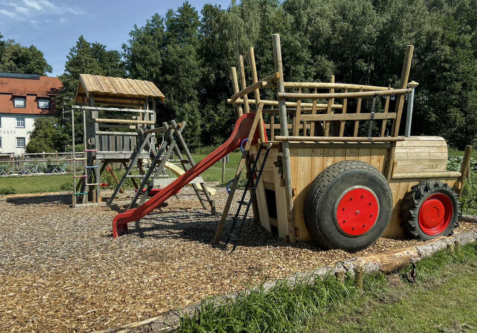 Abenteuerspielplatz aus Holz mit Klettergerüst, Rutsche und großen roten Rädern auf Kiesfläche
